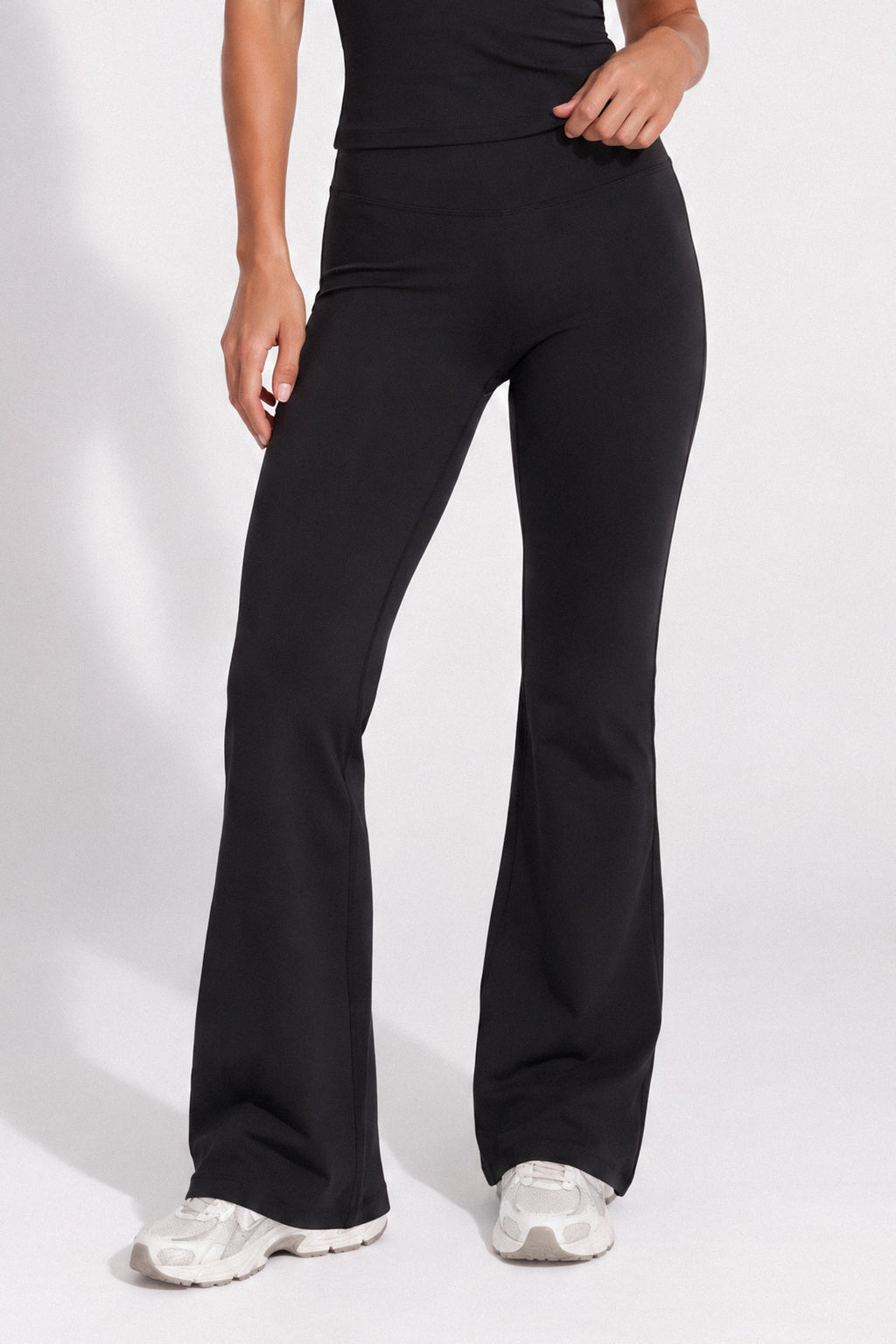Woman wearing black organic cotton high-waisted flare leggings and a matching cami top.